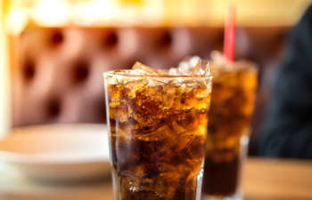 Two glasses of iced cola on a wooden table.