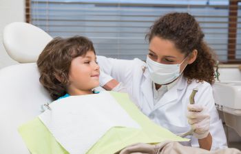 A pediatric dentist talking to a boy sitting in a dental chair.