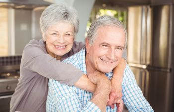 An older couple posing for a photo in the kitchen.