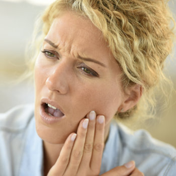 middle aged woman holds her cheek in pain