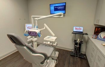 A dentist's office with a tv monitor and a dental chair.
