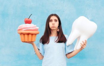 A woman stands holding a large fake cupcake in one hand and a large fake tooth in the other.