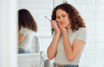 A young woman holding a toothbrush in her hand and pressing her jaw due to the pain she felt while brushing