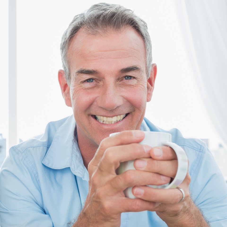 Smiling middle-aged man with a cup of coffee, looking at the camera