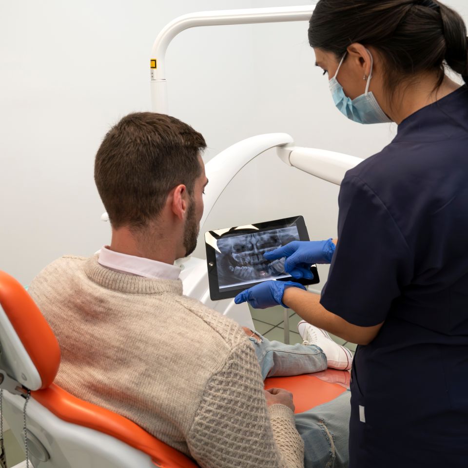 A dentist shows a dental X-ray on a tablet to a seated male patient in a dental clinic.