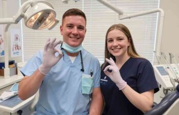 Smiling dental team poses in treatment room beside chair.